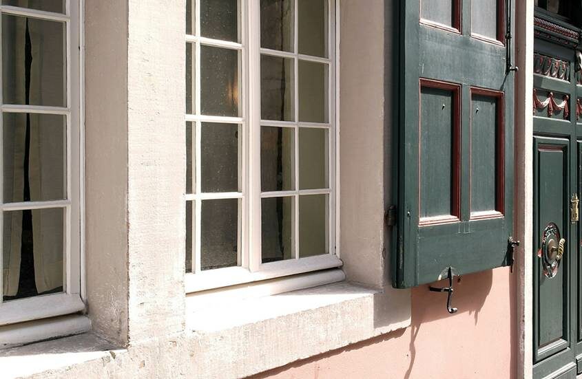 Nahaufnahme einer Hauswand mit zwei Fenstern in weißen Rahmen und einer grünen Doppelflügeltür